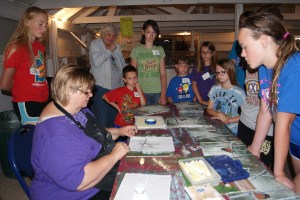 Painter, Connie Buskohl-Barney shares step by step instructions on using a pattern to create the robin in the woods picture while the 4-H members look at examples of the finished product. Taking part in the acrylic painting workshop were: Jayden Fleischman, Mary Tomes,  Connor Davis, Riley Davis, Miranda Bracht, Josie Richards, Alex Davis, and Anna Wakehouse.  Photo Courtesy of Mary Loftis.