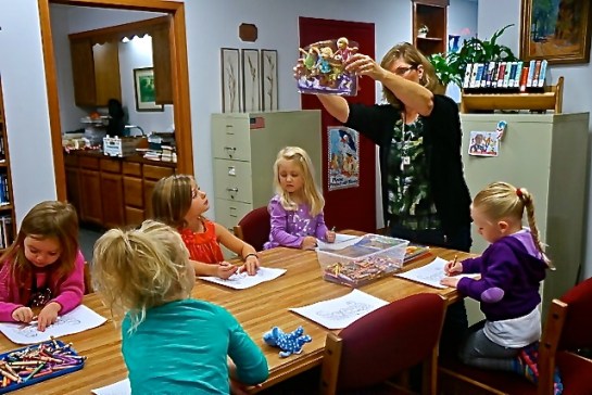 Oakland Library Director Rosa Schmidt leads this group of children in a coloring activity at the library. Pictured are back in pink, Laityn Johnson, Hilary Ray, Ava Johnson, Rosa,  Avery Christensen and Paisley Peterson. Photo Credit/Denise Gilliland, Editor and Chief, Kat Country Hub.