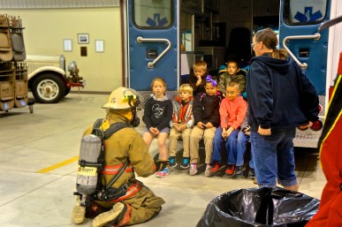 Jesse Raabe, left, a member of the Lyons Fire Department, shows the kids what a fireman looks like in his gear. Angela Whitley, right, describes the gear to them and what it does to protect the fireman. Photo Credit/Denise Gilliland, Editor and Chief, Kat Country Hub.
