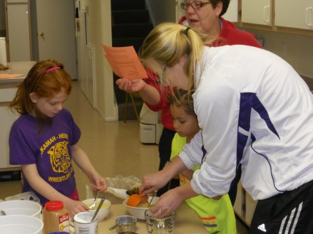 Izzy Connealy and Lily Willing get help making muffins from Jessica Fleischman while 4-H leader, Kim Jackson reads the recipe. The Flying Needs 4-H Club made apple and banana muffins which were shared during Burt County 4-H Week with the residents of the Golden Living Center, the Methodist Church coffee hour and the Extension Office. Photo Credit/Mary Loftis.