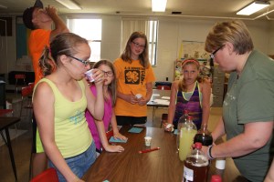 4-H/FFA Livestock Quality Assurance Training included a session on the importance of reading medication labels. This lesson was emphasized by having the participants try to identify what was in the beverage bottles by using the information available on the bottle and tasting and smelling the liquids. These Logan Valley Clovers 4-H members resort to tasting the liquids as the labeling was often incomplete. Hailey Miller of Lyons; Lyndsey Johnson of Oakland, Brent Miller of Lyons (behind); Elise Anderson of Lyons and Avery Bacon of Lyons take turns trying the different beverages as Tess Johnson of Oakland helped serve them. Photo Credit/Mary Loftis.